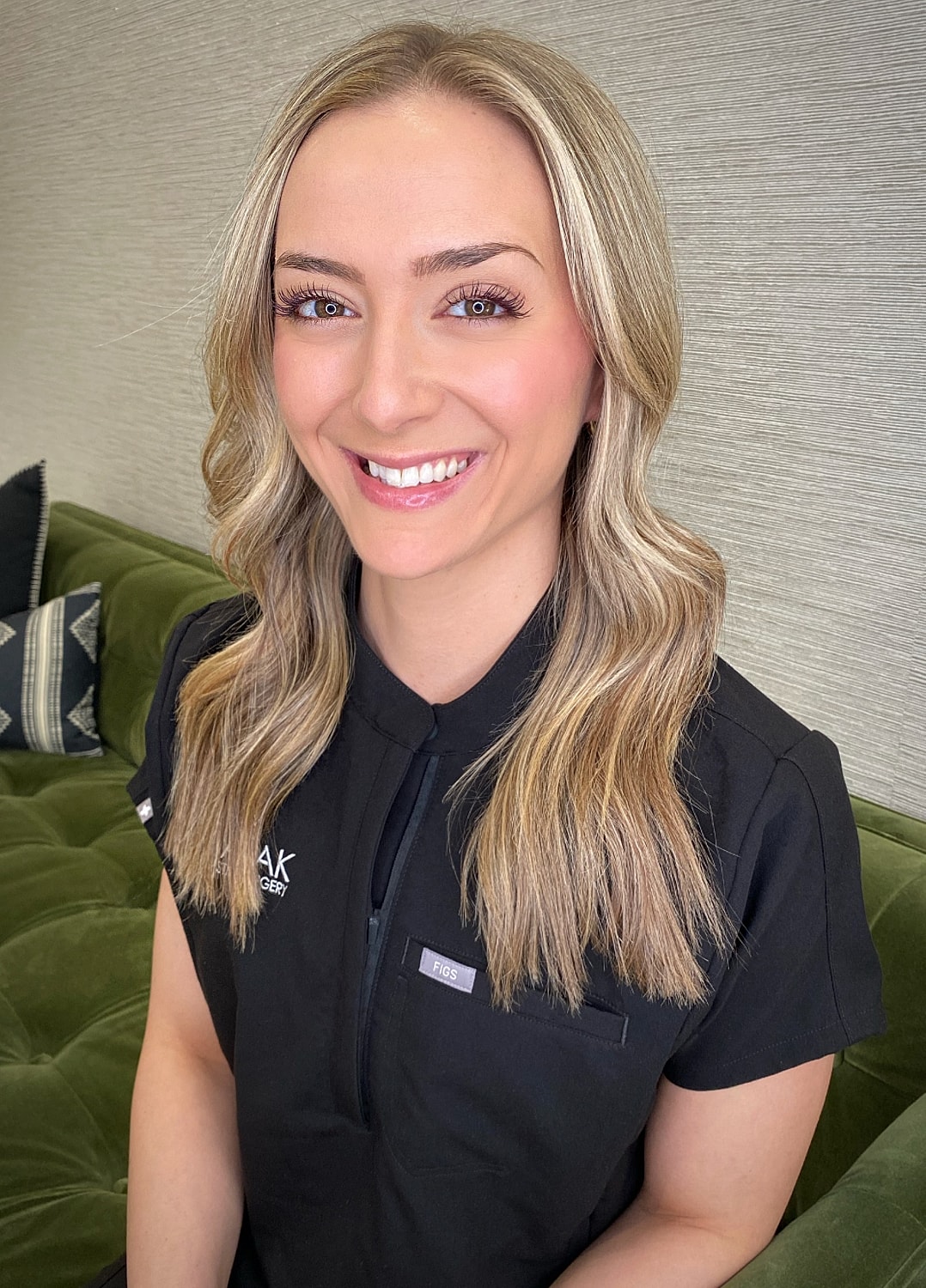 Smiling woman in medical attire against green background.