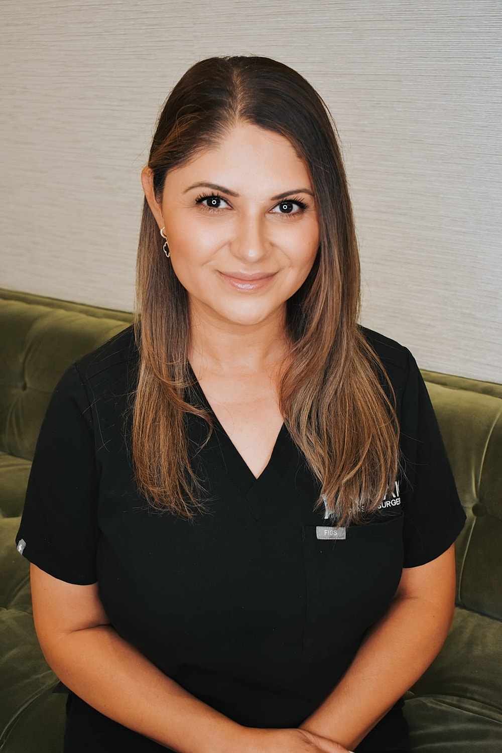 Smiling woman in medical attire seated on couch.