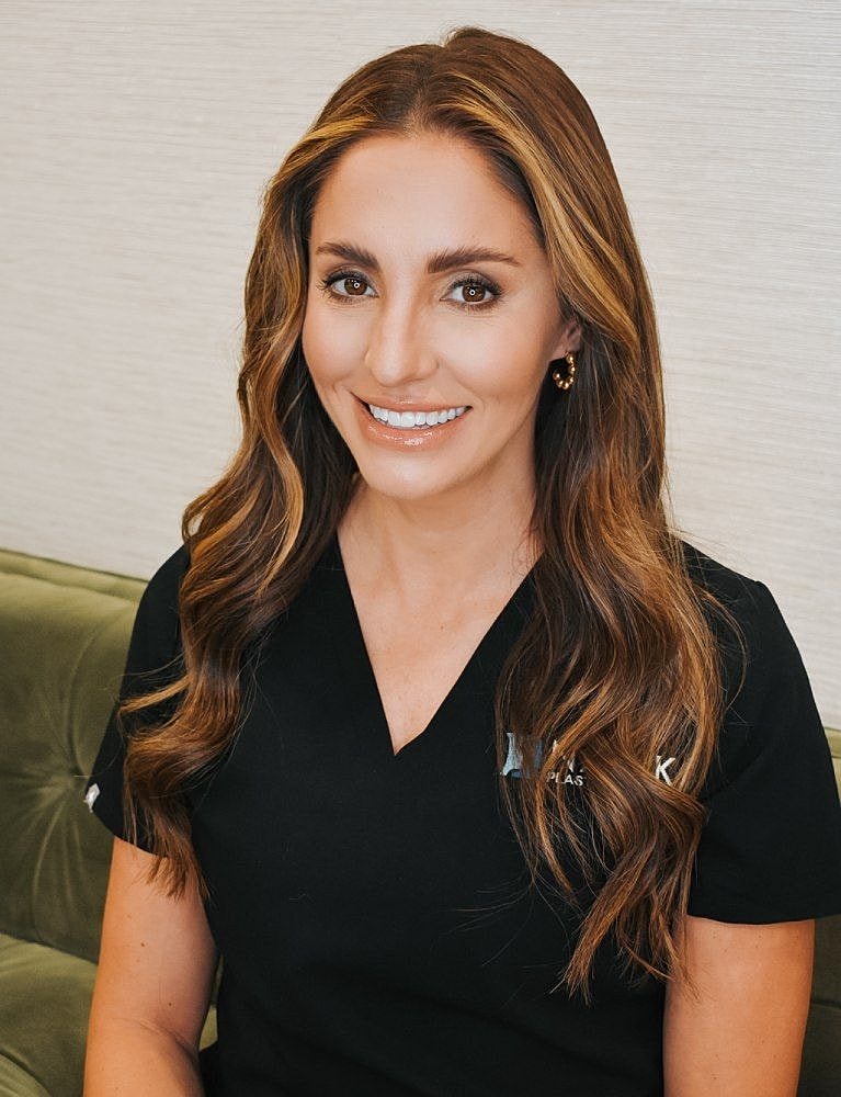 Smiling woman in medical scrubs, seated indoors.