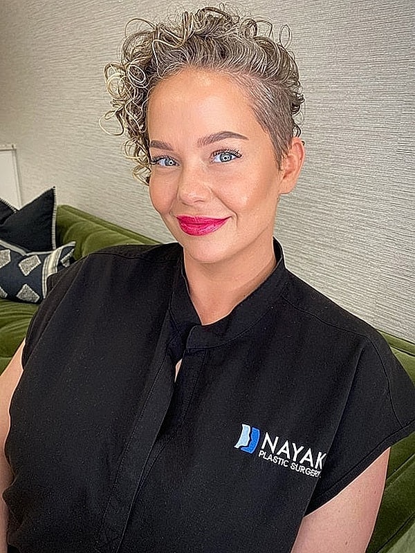 Smiling woman in medical attire, plastic surgery setting.