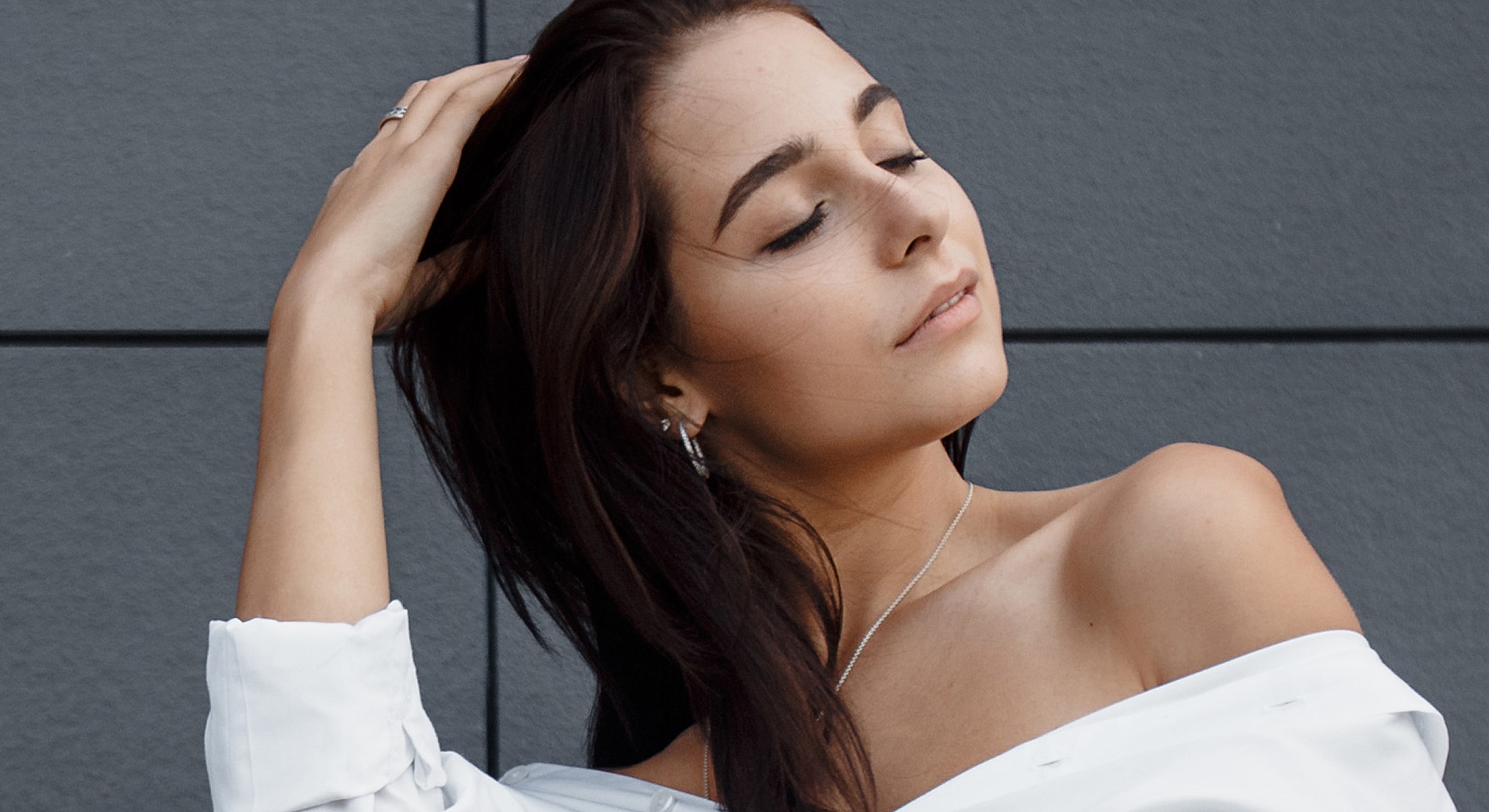 Woman posing with hair, wearing an off-shoulder top.